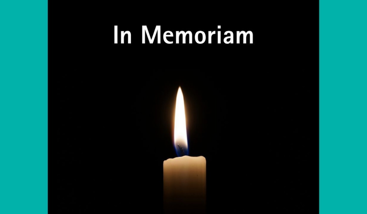 Close up image of the top of a lit candle with the flame shown against a dark background and the words In Memoriam written above in white text.